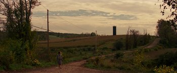 Movie still from “A Quiet Place” (2018), directed by John Krasinski – A person walking on a dirt road near a field; Extreme Wide shot, High angle