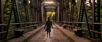 Movie still from “A Quiet Place” (2018), directed by John Krasinski – A woman is walking across a bridge in the sunlight; Wide shot, Over the shoulder angle