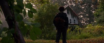 Movie still from “A Quiet Place” (2018), directed by John Krasinski – A person standing in front of a house with a teddy bear; Wide shot, Low angle