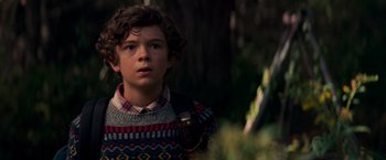 Movie still from “A Quiet Place” (2018), directed by John Krasinski – A young boy in a sweater is standing in the woods; Close Up shot, Over the shoulder angle