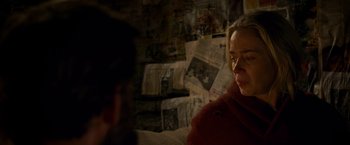 Movie still from “A Quiet Place” (2018), directed by John Krasinski – A woman sitting on a bed in front of a wall covered in newspapers; Close Up shot, Over the shoulder angle