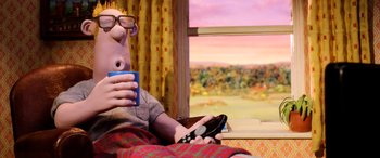 Movie still from “A Shaun the Sheep Movie: Farmageddon” (2019), directed by Will Becher – A man sitting in a chair holding a remote control and drinking a cup; Medium shot, Over the shoulder angle