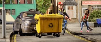 Movie still from “A Shaun the Sheep Movie: Farmageddon” (2019), directed by Will Becher – A man riding a bike next to a yellow dumpster; Wide shot, High angle