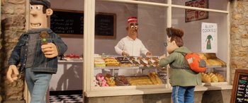 Movie still from “A Shaun the Sheep Movie: Farmageddon” (2019), directed by Will Becher – A man is behind the counter of a donut shop; Medium shot, Over the shoulder angle