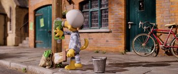 Movie still from “A Shaun the Sheep Movie: Farmageddon” (2019), directed by Will Becher – A statue of homer simpson is standing next to a bucket; Wide shot, Low angle