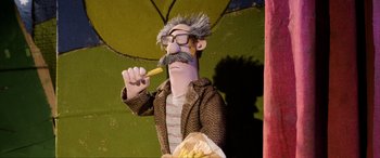 Movie still from “A Shaun the Sheep Movie: Farmageddon” (2019), directed by Will Becher – A man with a beard and glasses holding a piece of food; Medium shot, Low angle