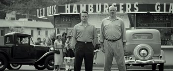 Movie still from “The Founder” (2016), directed by John Lee Hancock – A couple of men standing next to each other on the street; Medium shot, Low angle