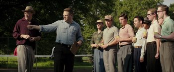 Movie still from “The Founder” (2016), directed by John Lee Hancock – A group of men standing next to each other on top of a field; Medium shot, Over the shoulder angle