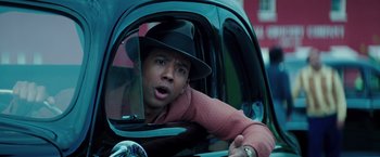 Movie still from “The Founder” (2016), directed by John Lee Hancock – A man wearing a black hat is in a car looking into a mirror; Close Up shot, High angle