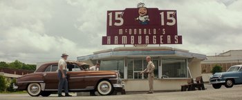 Movie still from “The Founder” (2016), directed by John Lee Hancock – A man standing next to an old car outside of a hamburger restaurant; Extreme Wide shot, Low angle