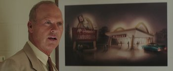 Movie still from “The Founder” (2016), directed by John Lee Hancock – A man standing in front of a picture of a hamburger restaurant; Close Up shot, Over the shoulder angle