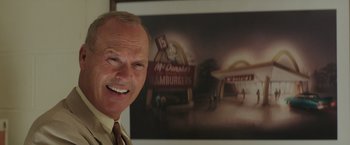 Movie still from “The Founder” (2016), directed by John Lee Hancock – An older man in front of a picture of a hamburger restaurant; Close Up shot, Over the shoulder angle