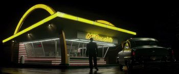 Movie still from “The Founder” (2016), directed by John Lee Hancock – A man standing in front of a mcdonald's restaurant at night; Extreme Wide shot, Low angle