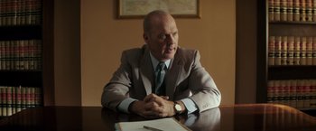 Movie still from “The Founder” (2016), directed by John Lee Hancock – A man sitting at a table in front of papers and a watch; Medium shot, Over the shoulder angle