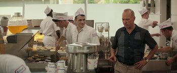 Movie still from “The Founder” (2016), directed by John Lee Hancock – A group of men standing in a kitchen preparing food; Medium shot, Over the shoulder angle