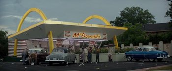 Movie still from “The Founder” (2016), directed by John Lee Hancock – A group of people standing outside of a mcdonald's restaurant; Extreme Wide shot, High angle