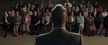 Movie still from “The Founder” (2016), directed by John Lee Hancock – A group of people sitting and standing in front of a man; Wide shot, High angle