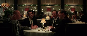 Movie still from “The Founder” (2016), directed by John Lee Hancock – A group of men sitting at a table in front of a lamp; Medium shot, Over the shoulder angle