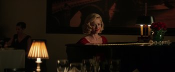 Movie still from “The Founder” (2016), directed by John Lee Hancock – A woman in a red dress sitting at a piano in a room; Medium shot, Over the shoulder angle