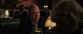 Movie still from “The Founder” (2016), directed by John Lee Hancock – A man sitting at a table with a glass of wine in front of him; Close Up shot, Over the shoulder angle