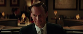 Movie still from “The Founder” (2016), directed by John Lee Hancock – A man in a black suit and a white tie; Close Up shot, Over the shoulder angle