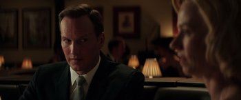 Movie still from “The Founder” (2016), directed by John Lee Hancock – A man in a suit and tie sitting in front of a lamp; Close Up shot, Over the shoulder angle