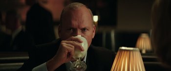 Movie still from “The Founder” (2016), directed by John Lee Hancock – A man in a black suit drinking a glass of wine; Close Up shot, Over the shoulder angle