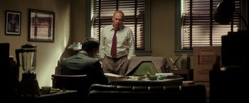 Movie still from “The Founder” (2016), directed by John Lee Hancock – A man standing in front of another man in front of a window; Medium shot, Low angle