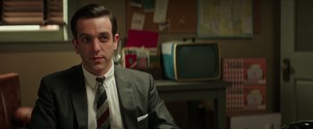 Movie still from “The Founder” (2016), directed by John Lee Hancock – A man wearing a suit and tie sitting in front of a television; Close Up shot, Over the shoulder angle