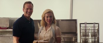 Movie still from “The Founder” (2016), directed by John Lee Hancock – A woman holding a cake in front of a man; Medium shot, Low angle