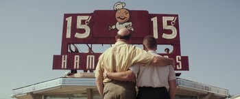 Movie still from “The Founder” (2016), directed by John Lee Hancock – Two men standing next to each other in front of a restaurant sign; Medium shot, Low angle