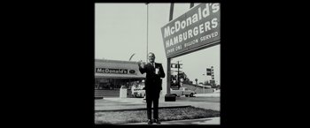 Movie still from “The Founder” (2016), directed by John Lee Hancock – A man standing in front of a mcdonald's sign; Wide shot, Low angle