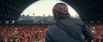 Movie still from “A Star Is Born” (2018), directed by Bradley Cooper – A man with a guitar in front of a crowd; Medium shot, Over the shoulder angle