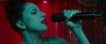 Movie still from “A Star Is Born” (2018), directed by Bradley Cooper – A woman is holding a microphone up to her mouth; Close Up shot, Overhead angle