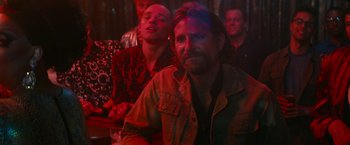 Movie still from “A Star Is Born” (2018), directed by Bradley Cooper – A man sitting next to another man in a bar; Close Up shot, Over the shoulder angle
