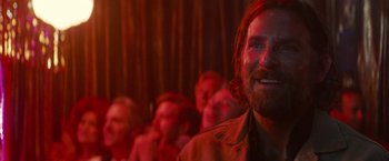 Movie still from “A Star Is Born” (2018), directed by Bradley Cooper – A person smiling in front of other people; Close Up shot, Over the shoulder angle