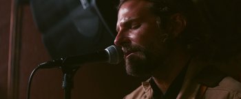 Movie still from “A Star Is Born” (2018), directed by Bradley Cooper – A person singing on a microphone; Close Up shot, Over the shoulder angle
