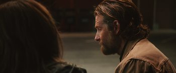 Movie still from “A Star Is Born” (2018), directed by Bradley Cooper – A man with long hair and a goatee is talking to a woman; Close Up shot, Over the shoulder angle