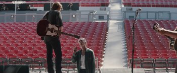 Movie still from “A Star Is Born” (2018), directed by Bradley Cooper – A man standing on a stage next to another man; Wide shot, Low angle