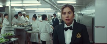 Movie still from “A Star Is Born” (2018), directed by Bradley Cooper – A woman wearing a suit and bow tie in front of a group of people; Close Up shot, Over the shoulder angle