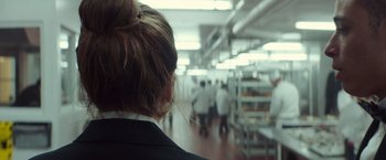 Movie still from “A Star Is Born” (2018), directed by Bradley Cooper – A woman in a white lab coat looking at some people in a kitchen; Close Up shot, Over the shoulder angle