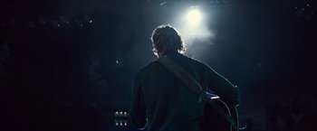 Movie still from “A Star Is Born” (2018), directed by Bradley Cooper – A man playing a guitar in a dark room; Medium shot, Over the shoulder angle
