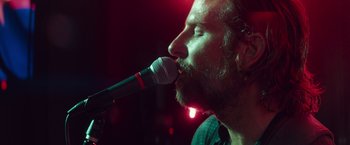 Movie still from “A Star Is Born” (2018), directed by Bradley Cooper – A man with a beard is singing into a microphone; Close Up shot, Low angle