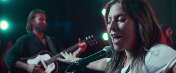 Movie still from “A Star Is Born” (2018), directed by Bradley Cooper – A woman singing into a microphone while holding a guitar; Close Up shot, Low angle