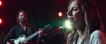 Movie still from “A Star Is Born” (2018), directed by Bradley Cooper – A woman singing into a microphone in front of an electric guitar; Close Up shot, Low angle