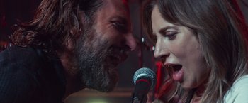 Movie still from “A Star Is Born” (2018), directed by Bradley Cooper – A man and a woman singing into a microphone; Close Up shot, Over the shoulder angle