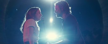 Movie still from “A Star Is Born” (2018), directed by Bradley Cooper – A man and a woman sing into microphones in front of a bright light; Close Up shot, Low angle