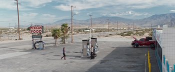 Movie still from “A Star Is Born” (2018), directed by Bradley Cooper – A woman walking in a parking lot next to a gas station; Extreme Wide shot, High angle