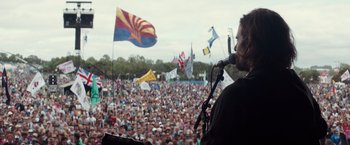 Movie still from “A Star Is Born” (2018), directed by Bradley Cooper – A crowd of people are gathered in a field; Medium shot, Over the shoulder angle
