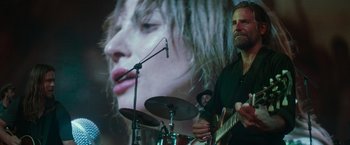 Movie still from “A Star Is Born” (2018), directed by Bradley Cooper – A man playing drums in front of a microphone; Medium shot, Over the shoulder angle